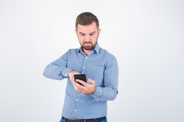 Photo gratuite portrait de jeune homme regardant téléphone mobile en chemise, jeans et à la vue de face ciblée