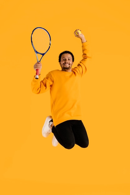 Portrait jeune homme sautant avec raquette de tennis