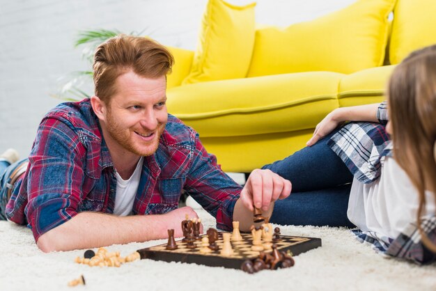 Portrait d&#39;un jeune homme souriant, couché sur un tapis, jouant aux échecs avec sa petite amie