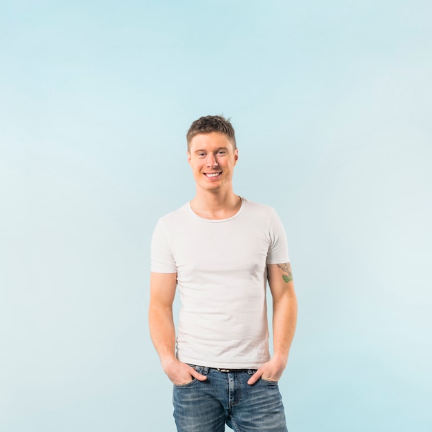 Portrait d&#39;un jeune homme souriant avec ses deux mains dans la poche sur fond bleu