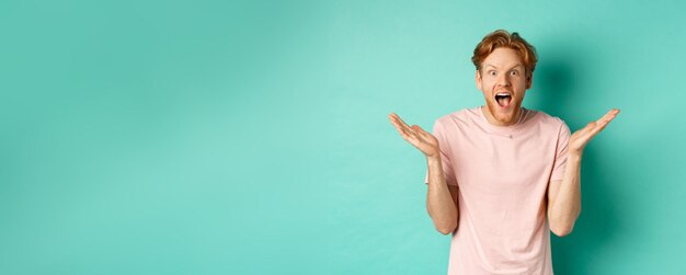 Photo gratuite portrait d'un jeune homme surpris et heureux aux cheveux roux, écartant les mains sur le côté et haletant d'admiration