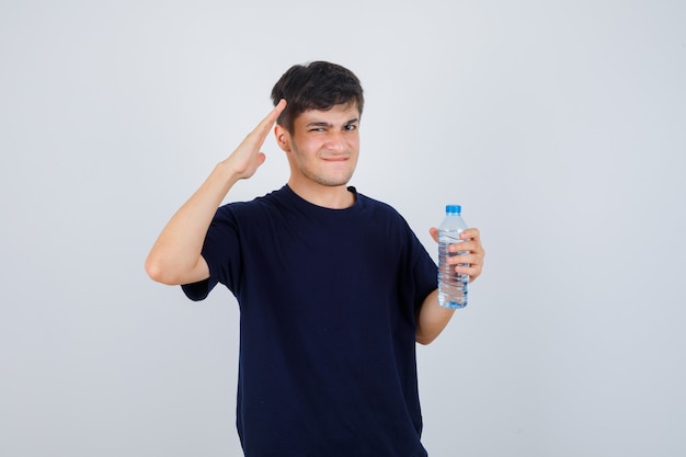 Portrait de jeune homme tenant une bouteille d'eau, montrant le geste de salut, pincer les lèvres tout en fronçant les sourcils en t-shirt noir et à la vue de face confuse