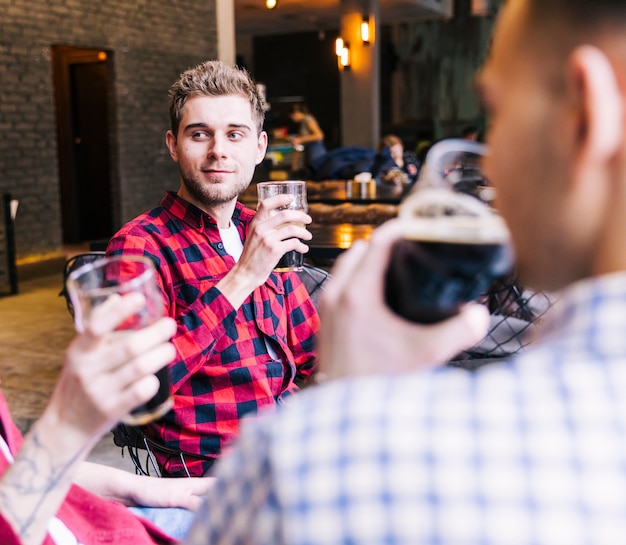 Photo gratuite portrait d'un jeune homme tenant un verre de bière assis avec son ami