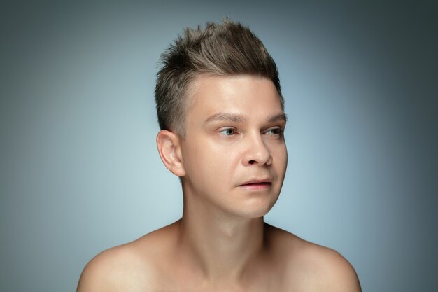 Portrait de jeune homme torse nu isolé sur mur gris. Modèle masculin en bonne santé caucasien regardant sur le côté et posant. Concept de la santé et de la beauté des hommes, des soins personnels, des soins du corps et de la peau.