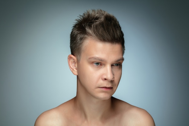 Portrait de jeune homme torse nu isolé sur mur gris. Modèle masculin en bonne santé caucasien regardant sur le côté et posant. Concept de la santé et de la beauté des hommes, des soins personnels, des soins du corps et de la peau.