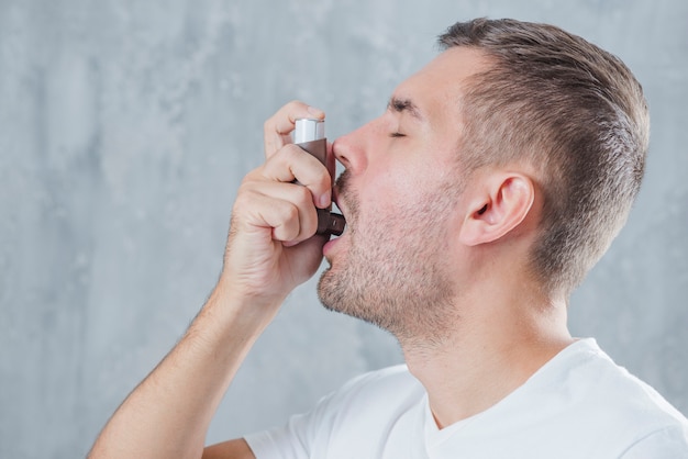 Portrait d'un jeune homme utilisant l'asthme inhalateur sur fond gris