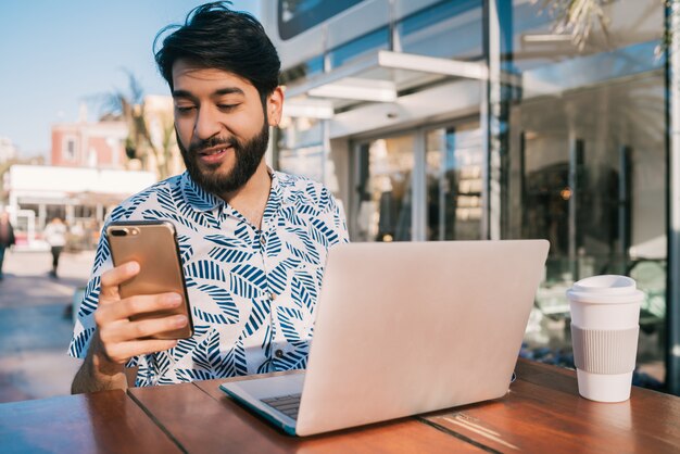 Portrait de jeune homme utilisant son ordinateur portable et utilisant son téléphone portable alors qu'il était assis dans un café.