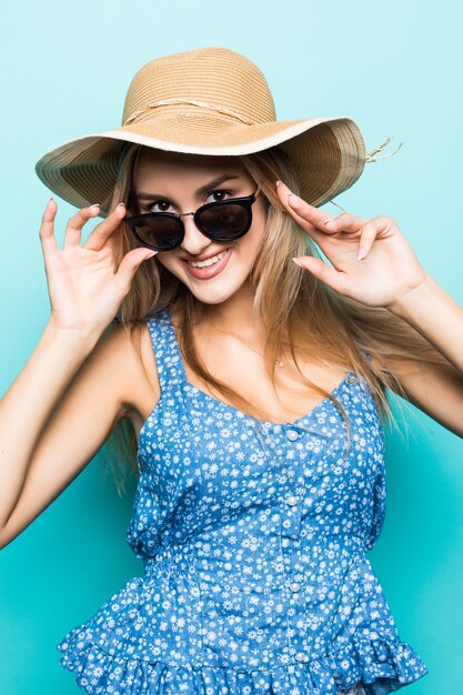 Portrait de jeune jolie femme en chapeau d'été et lunettes de soleil isolé sur fond bleu