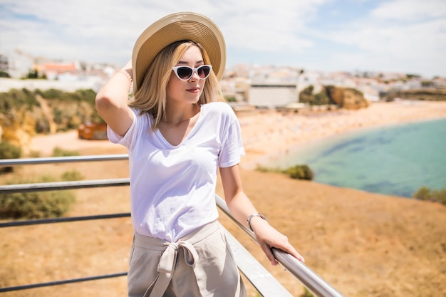 Photo gratuite portrait de jeune jolie femme avec chapeau et lunettes de soleil sur le dessus près de la plage