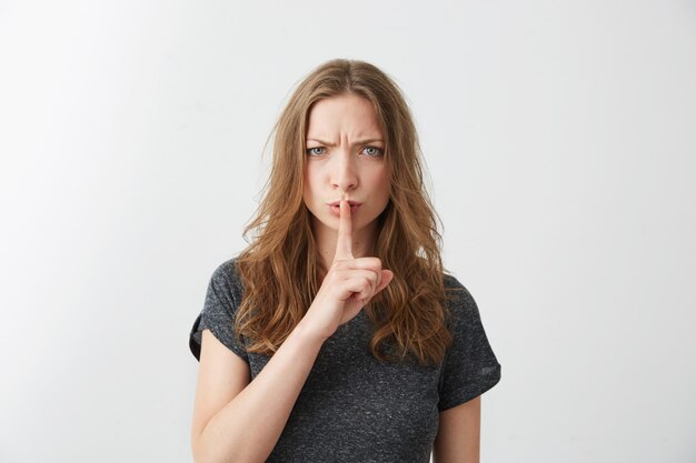 Portrait de jeune jolie fille fronçant les sourcils montrant directement garder le silence.