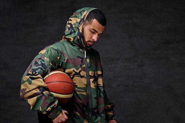 Portrait d'un jeune joueur de basket-ball de rue afro-américain dans une veste de camouflage. Isolé sur fond sombre.