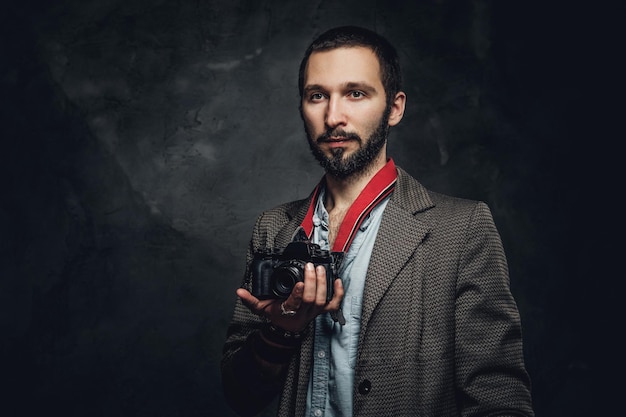 Photo gratuite portrait de jeune journaliste barbu avec appareil photo au studio photo sombre.