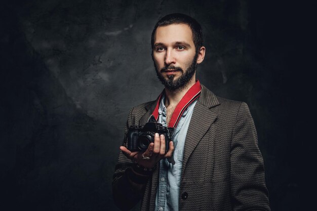 Portrait de jeune journaliste barbu avec appareil photo au studio photo sombre.