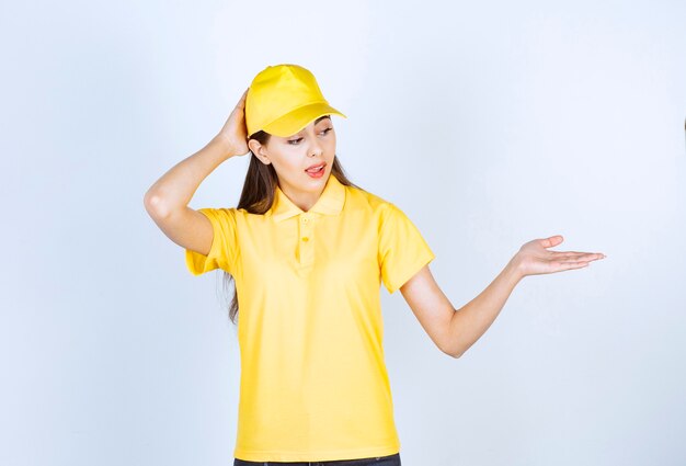 Portrait de jeune livreuse en casquette jaune debout sur blanc.