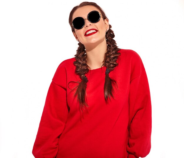 Portrait de jeune modèle femme souriante heureuse avec maquillage lumineux et lèvres colorées avec deux nattes et lunettes de soleil dans des vêtements d'été rouges isolés.