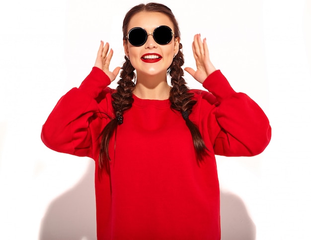 Portrait de jeune modèle femme souriante heureuse avec maquillage lumineux et lèvres colorées avec deux nattes et lunettes de soleil dans des vêtements d'été rouges isolés.