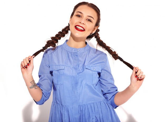 Portrait de jeune modèle femme souriante heureuse avec maquillage lumineux et lèvres rouges avec deux nattes en mains en été robe bleue colorée isolée