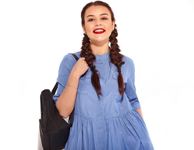 Portrait de jeune modèle femme souriante heureuse avec maquillage lumineux et lèvres rouges avec deux nattes en mains en été robe bleue colorée et sac à dos isolé.