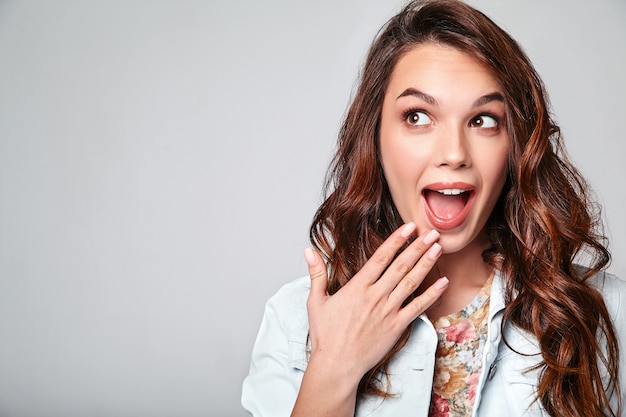 Portrait de jeune modèle riant élégant en vêtements d'été décontractés colorés avec du maquillage naturel sur gris