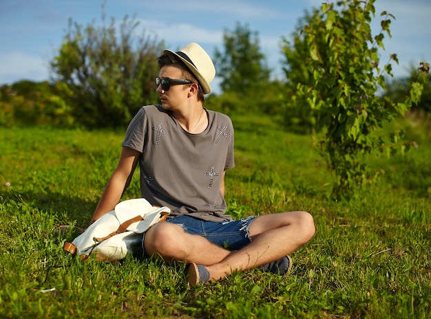 portrait, de, jeune, séduisant, moderne, élégant, homme, dans, désinvolte, tissu, dans, chapeau, dans, lunettes, séance, dans parc, dans, herbe verte