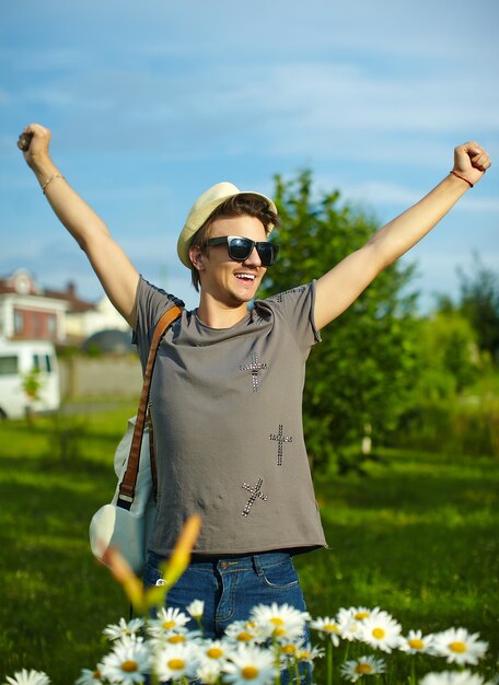 portrait, de, jeune, séduisant, sourire, moderne, élégant, homme, dans, désinvolte, chapeau, dans, lunettes, dans parc, à, vif, coloré, fleurs, dans, camomille