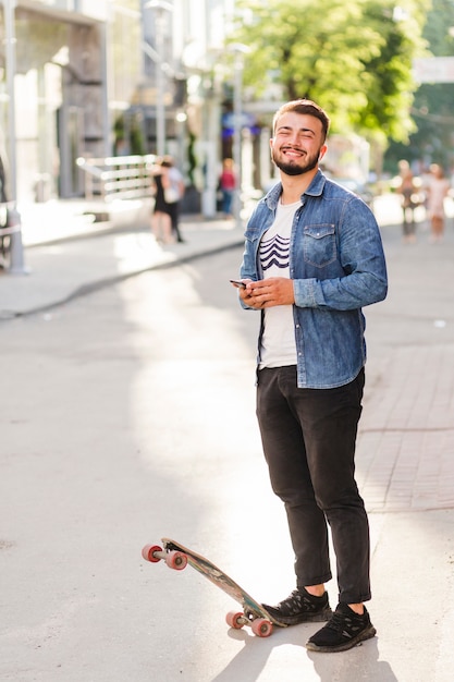 Portrait d&#39;un jeune skateur masculin souriant avec téléphone portable