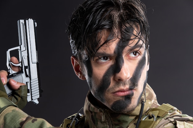 Portrait de jeune soldat en camouflage visant le pistolet sur mur sombre