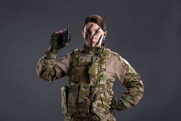 Portrait de jeune soldat en tenue de camouflage avec grenade sur mur sombre