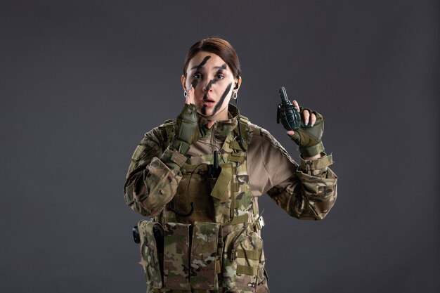 Portrait de jeune soldat en tenue de camouflage avec grenade sur ses mains mur sombre