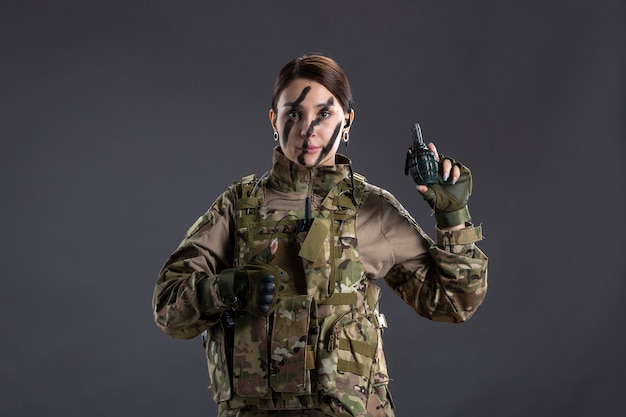 Portrait de jeune soldat en tenue de camouflage avec grenade sur ses mains mur sombre