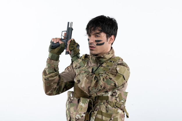 Portrait de jeune soldat en tenue de camouflage avec pistolet sur mur blanc