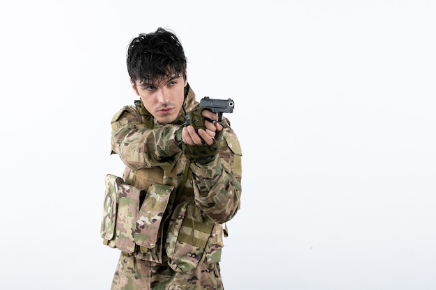 Portrait de jeune soldat en tenue de camouflage avec pistolet sur mur blanc