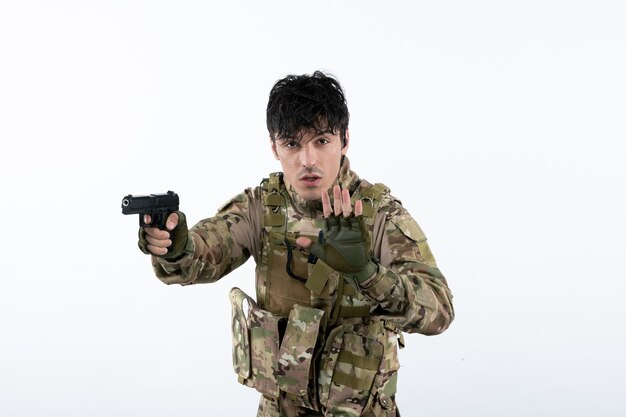 Portrait de jeune soldat en tenue de camouflage avec pistolet sur mur blanc