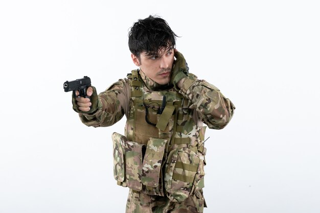 Portrait de jeune soldat en tenue de camouflage avec pistolet sur mur blanc
