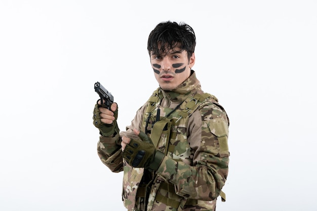 Portrait de jeune soldat en tenue de camouflage avec pistolet sur mur blanc