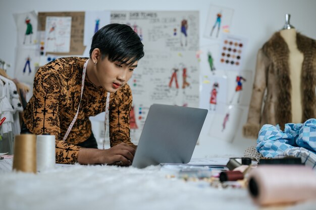 Portrait d'un jeune tailleur asiatique professionnel avec un ruban à mesurer sur le cou travaillant sur un ordinateur portable