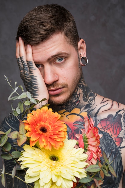 Portrait, jeune, tatoué, percé, tenant, fleurs, main, regarder appareil-photo