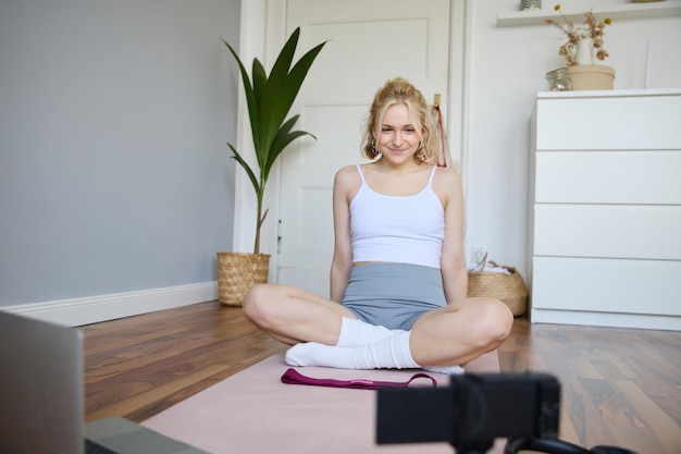 Photo gratuite portrait d'une jeune vloggeuse instructrice de fitness montrant des exercices sur une caméra qui l'enregistre assise