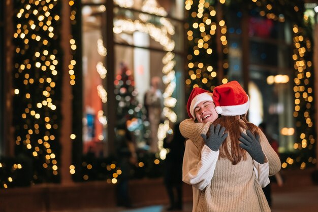 Portrait de jeunes amis mignons heureux étreignant les uns les autres et souriant en marchant à la veille de Noël à l'extérieur.