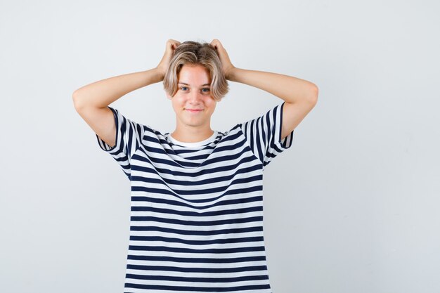 Portrait d'un joli garçon adolescent avec les mains sur la tête en t-shirt rayé et à la vue de face joyeuse