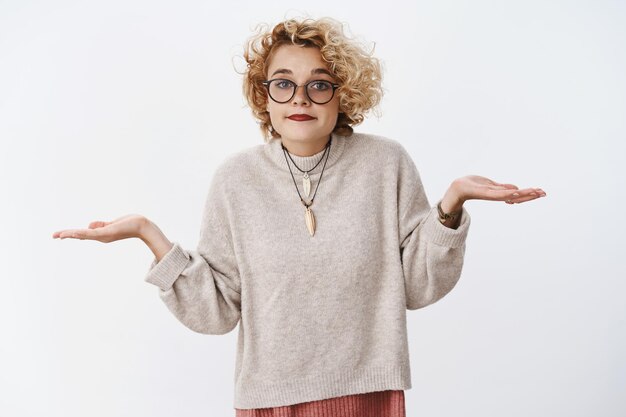 Portrait d'une jolie collègue blonde européenne indifférente et désemparée haussant les épaules avec les mains écartées sur le côté et un sourire narquois