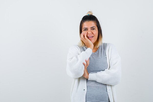 Portrait d'une jolie dame penchée sur la joue en t-shirt, cardigan et joyeuse vue de face