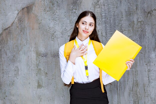 Portrait d'une jolie étudiante avec un cahier jaune posant devant la caméra. Photo de haute qualité