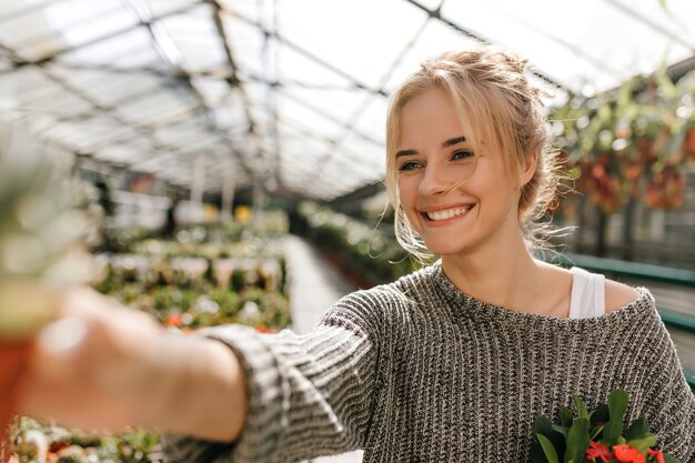 Portrait de jolie femme aux yeux verts avec le sourire pose en serre et détient la plante.