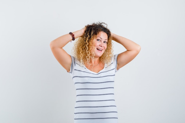 Portrait de jolie femme blonde gardant les mains sur la tête en t-shirt rayé et à la vue de face heureuse