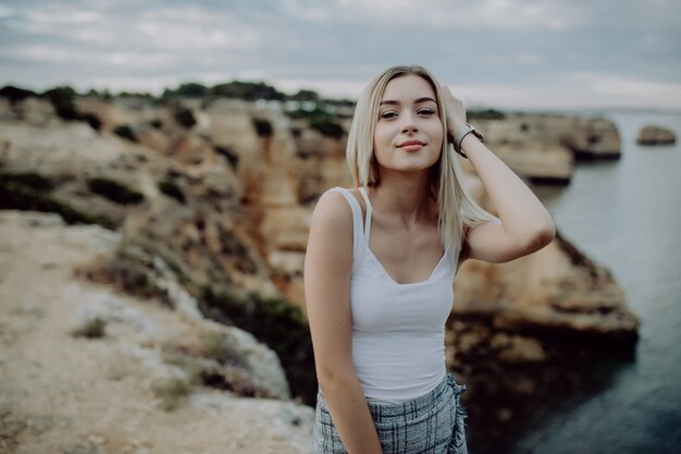 Portrait de jolie femme blonde posant sur une plage rocheuse avec un paysage de beauté.