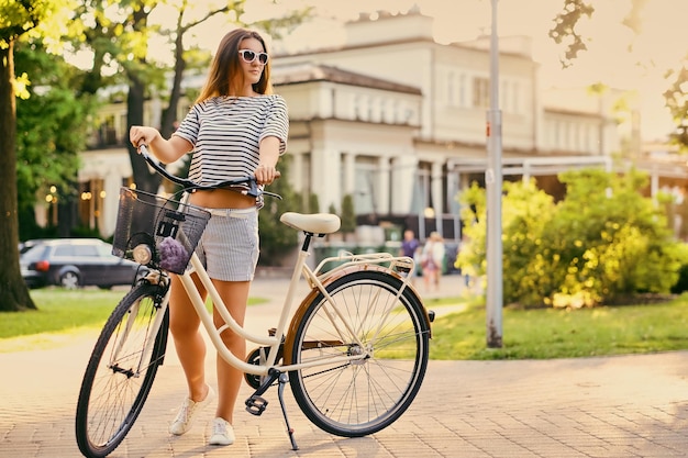 Portrait d'une jolie femme brune avec un vélo dans le parc de la ville.