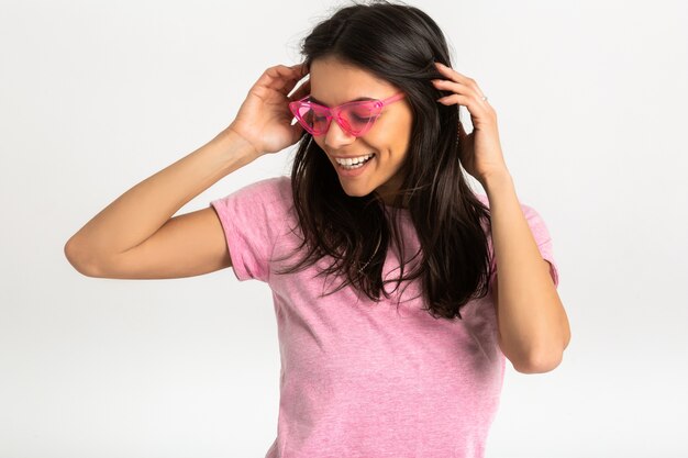 Portrait de jolie femme émotionnelle assez souriante en chemise rose et lunettes de soleil élégantes, pose positive isolée