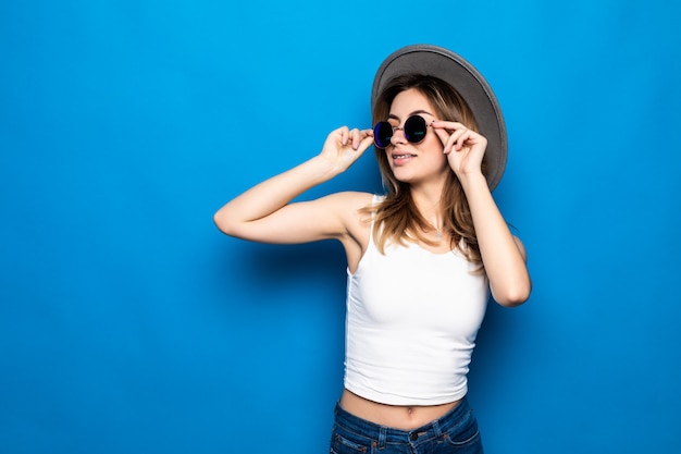 Portrait de jolie femme à lunettes de soleil et chapeau sur mur coloré bleu