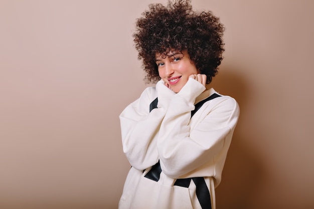 Portrait de jolie femme sensible aux cheveux courts bouclés habillé chemise blanche pose sur rose